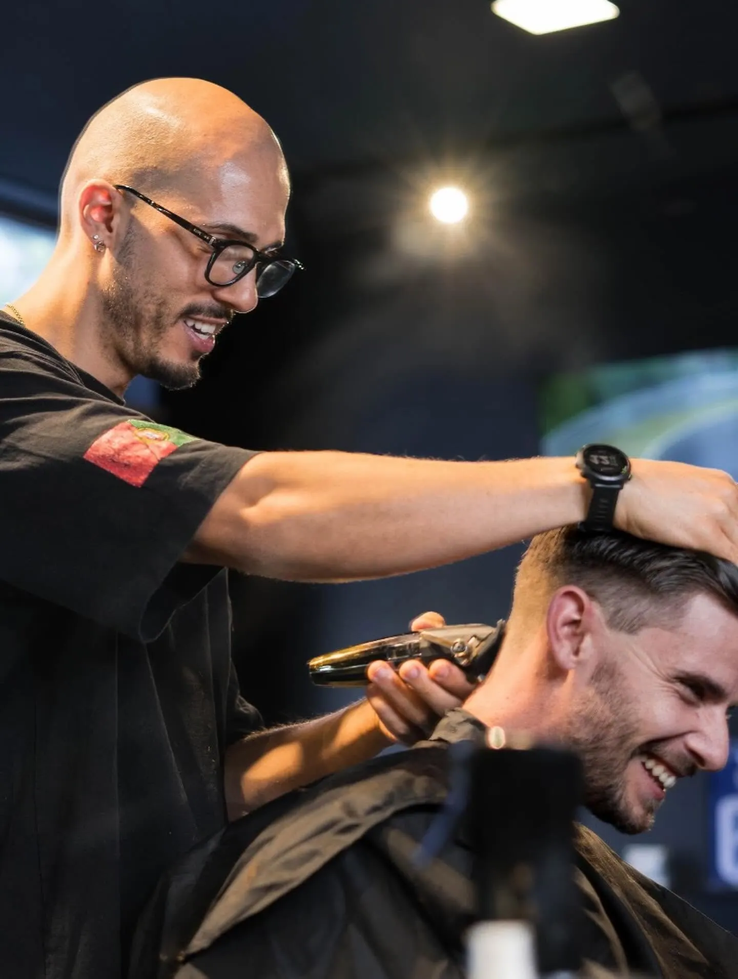Barbeiro a acertar a nuca de um cliente com a máquina, os dois a rir
